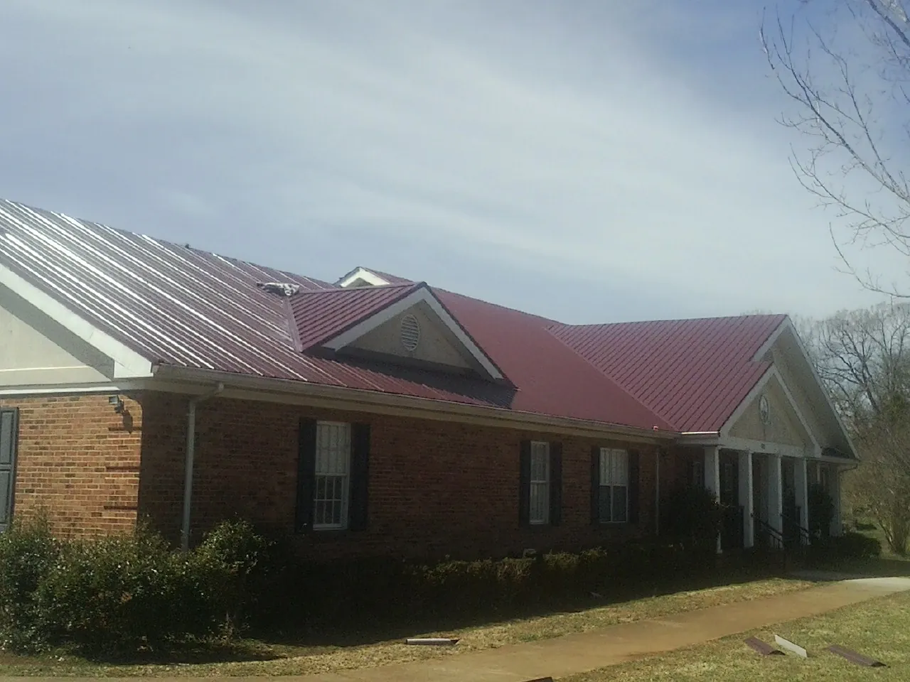 Red metal roof with gabled entries on a long brick building, from a Hail Damage Roof Repair job in Savannah